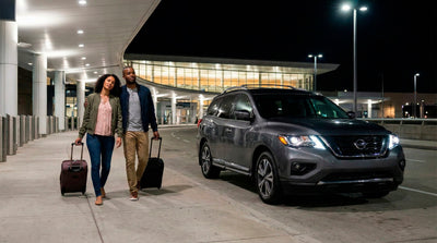 Couple walking with luggage towards their grey Nissan Pathfinder rental car at night at the airport.