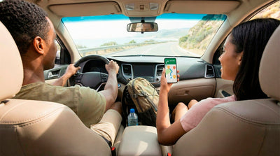 Passenger holding a smartphone displaying a navigation app inside a rental car during a road trip.