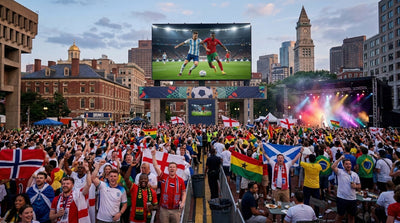 Football fans in Boston waving national flags and watching a match on a giant outdoor screen, capturing the FIFA World Cup 2026 fan festival atmosphere.
