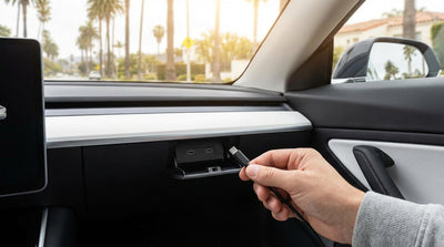 A hand plugging a USB-C cable into the console of a California car hire with a sunny road ahead
