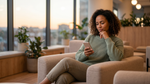 A woman checks her phone in a lounge, waiting for a car hire credit card deposit hold to release.