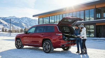 Couple loading skis into a red Jeep Grand Cherokee L car rental for a winter ski trip near Denver.