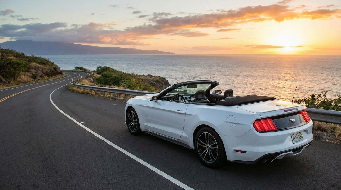 A white Ford Mustang convertible rental car is parked on a scenic coastal road in Maui during a beautiful sunset.