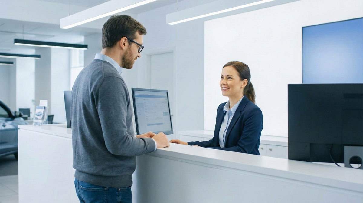 A customer talks to a friendly car rental agent at a desk, inquiring about renting a car without a security deposit or credit card hold.