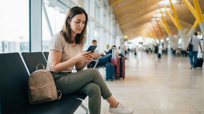 Traveler checking car rental quotes on a phone at the airport, reviewing taxes and fees for their car hire.