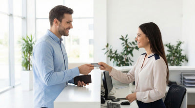 Man handing a new credit card to a car hire agent at a counter to update payment details during vehicle pick-up.