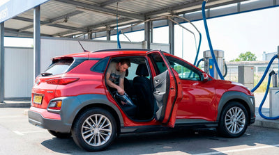 Man vacuuming the back seat of a red Hyundai Kona rental car at a self-service wash.