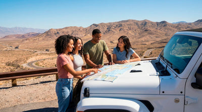 Group of friends checking a map on a Jeep hood during a cross-country road trip with a one-way car rental.