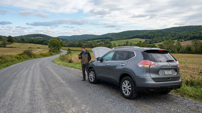 A broken-down car rental with its hood up on the side of a deserted, wooded road in Pennsylvania