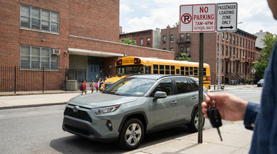 A car rental stopped near a school zone street sign on a tree-lined block in New York