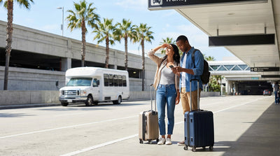 Passengers with luggage waiting at the LAX arrivals curb for a car rental shuttle in Los Angeles