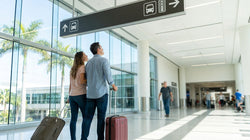 Travelers walking past overhead signs for the car rental shuttle inside an airport terminal in Miami