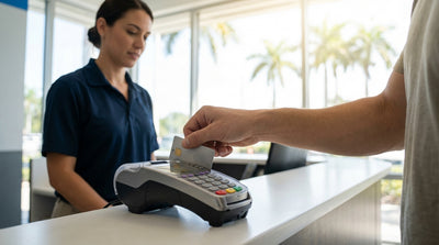 A person holding a credit card at a car hire counter with a sunny Florida backdrop visible through a window
