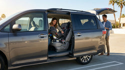 Parent buckling a toddler into a child seat inside a car rental parked on a sunny street in Texas