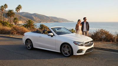 A silver Mercedes-Benz car rental parked on a cliff overlooking the sunny California coast and Pacific Ocean