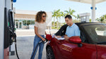 Person pumping gas into a white car rental at a sunny gas station in Miami
