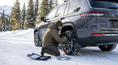 A car hire drives on a winding, snow-covered road through a pine forest in California