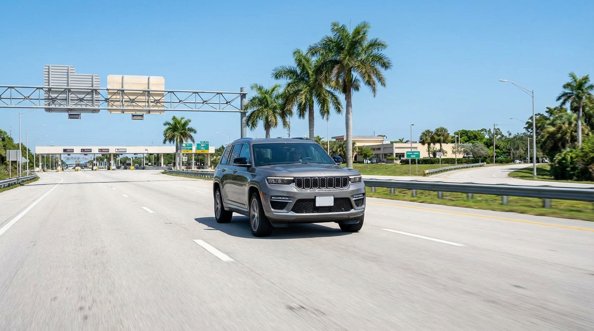 A silver car hire driving under an electronic toll gantry on a sunny highway in Florida lined with palm trees