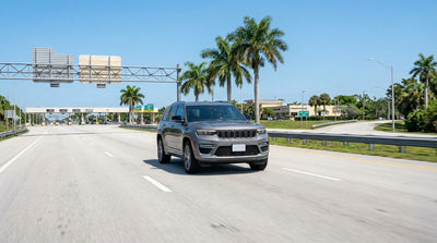 A silver car hire driving under an electronic toll gantry on a sunny highway in Florida lined with palm trees