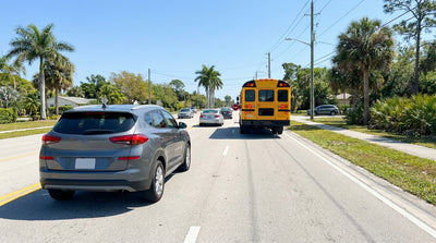 A car hire stopped for a yellow school bus with flashing red lights on a sunny road in Florida