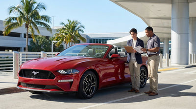 A convertible car rental driving down a sunny, palm-lined coastal highway in Florida