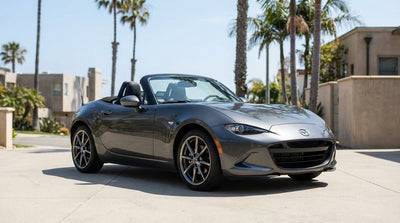 A silver convertible car rental driving along a sunny, winding coastal highway in California
