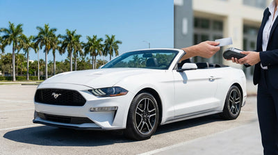 A person's hand holding car keys and a payment card for their car hire at a rental counter in Miami