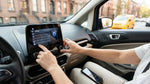 Person adjusting the infotainment screen of a car rental with New York streets visible through the window
