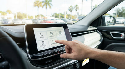 A driver's hand touches the dashboard screen of a car hire vehicle on a scenic California road trip