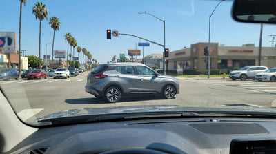 A car hire waiting at a traffic light on a sunny, palm-lined street in Los Angeles