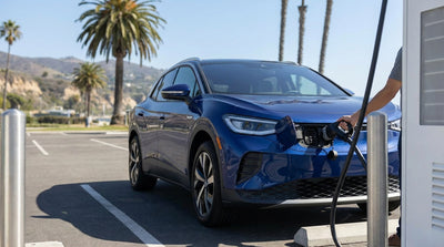 A person plugs a charging cable into a white electric car rental at a charging station in sunny California