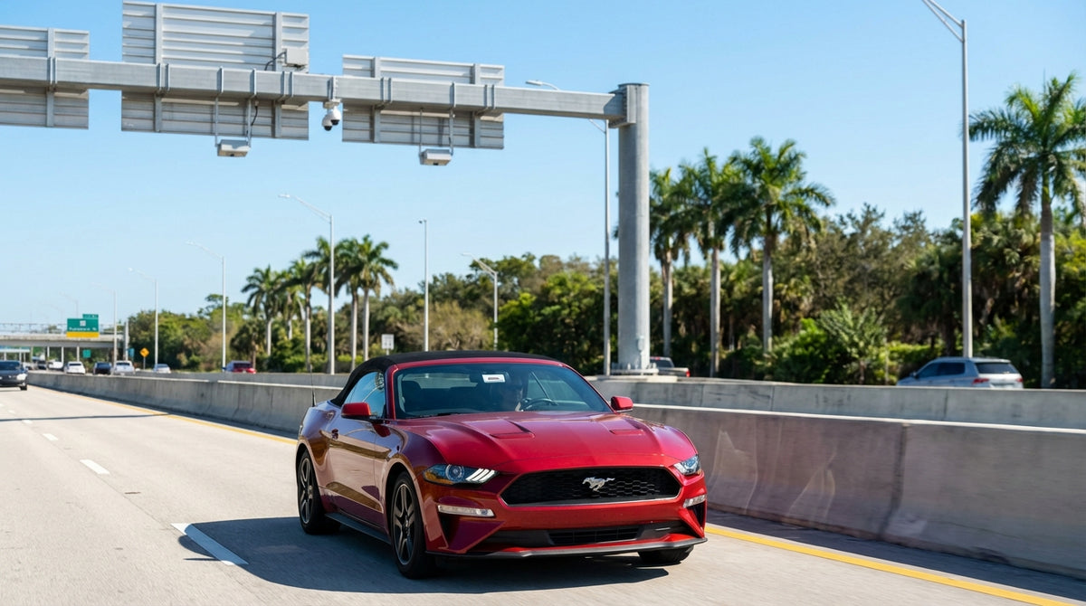 A white car rental drives under an electronic toll sign on the sunny Florida I-4 Express lanes