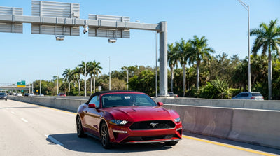 A white car rental drives under an electronic toll sign on the sunny Florida I-4 Express lanes