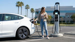 A white Tesla car rental plugged into an electric vehicle charging station on a sunny day in California