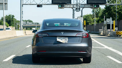 A white car hire drives through a toll booth on a bridge with the New York City skyline in the background