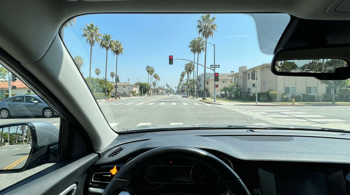 A car rental stopped at a red traffic light on a sunny, palm-lined street in Los Angeles