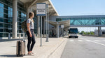 Travelers with luggage boarding a car rental shuttle bus at a New York airport terminal