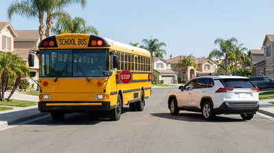 A car rental stops for a yellow school bus with flashing red lights on a sunny street in California