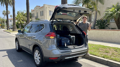A person loads luggage into the trunk of a car hire on a sunny, palm-lined street in Los Angeles