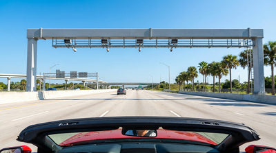 A white car rental drives under a cashless toll gantry on a palm-lined highway in Florida