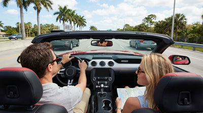 A convertible car rental driving down a sunny, palm-tree-lined coastal road in Florida