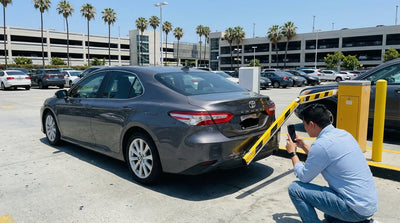 A parking barrier arm resting on the dented hood of a silver car hire in a Los Angeles garage