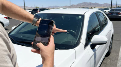 A person inspects the windscreen of a white car hire vehicle for chips in a sunny Las Vegas parking lot