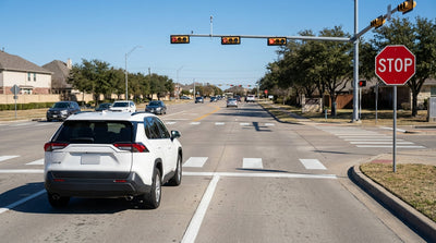 A car rental stopped at a red light in a right-turn slip lane at a sunny intersection in Texas