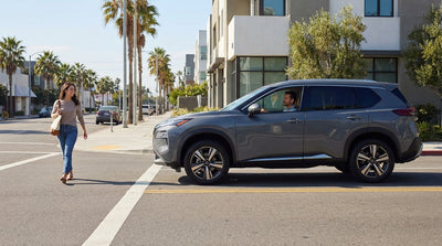 A car hire stops for a pedestrian at an unmarked crossing on a sunny, palm-lined California street