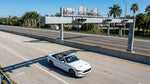 A white car rental passing under an electronic toll gantry on a sunny Florida highway