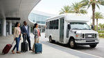 Passengers with luggage boarding a white car hire shuttle bus outside the Orlando airport terminal