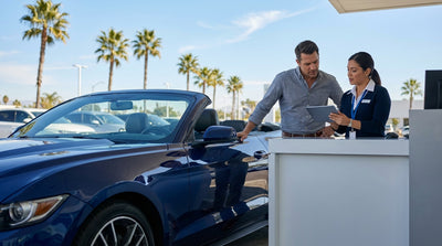A red convertible car hire drives along a sunny, winding coastal highway in California next to the Pacific Ocean
