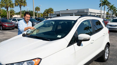 A person inspecting the license plate of a white sedan from a Florida car rental service