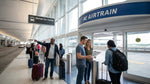 Travelers with luggage walking past a car hire sign inside San Francisco airport Terminal 3